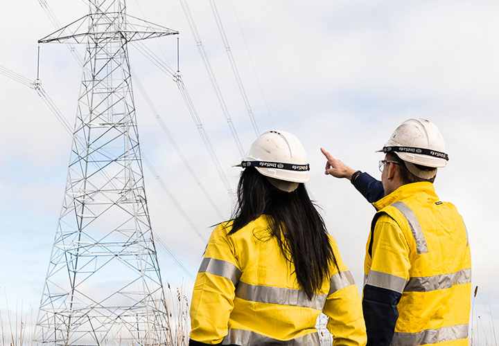 Two people in high vis discussing a powerline in the distance