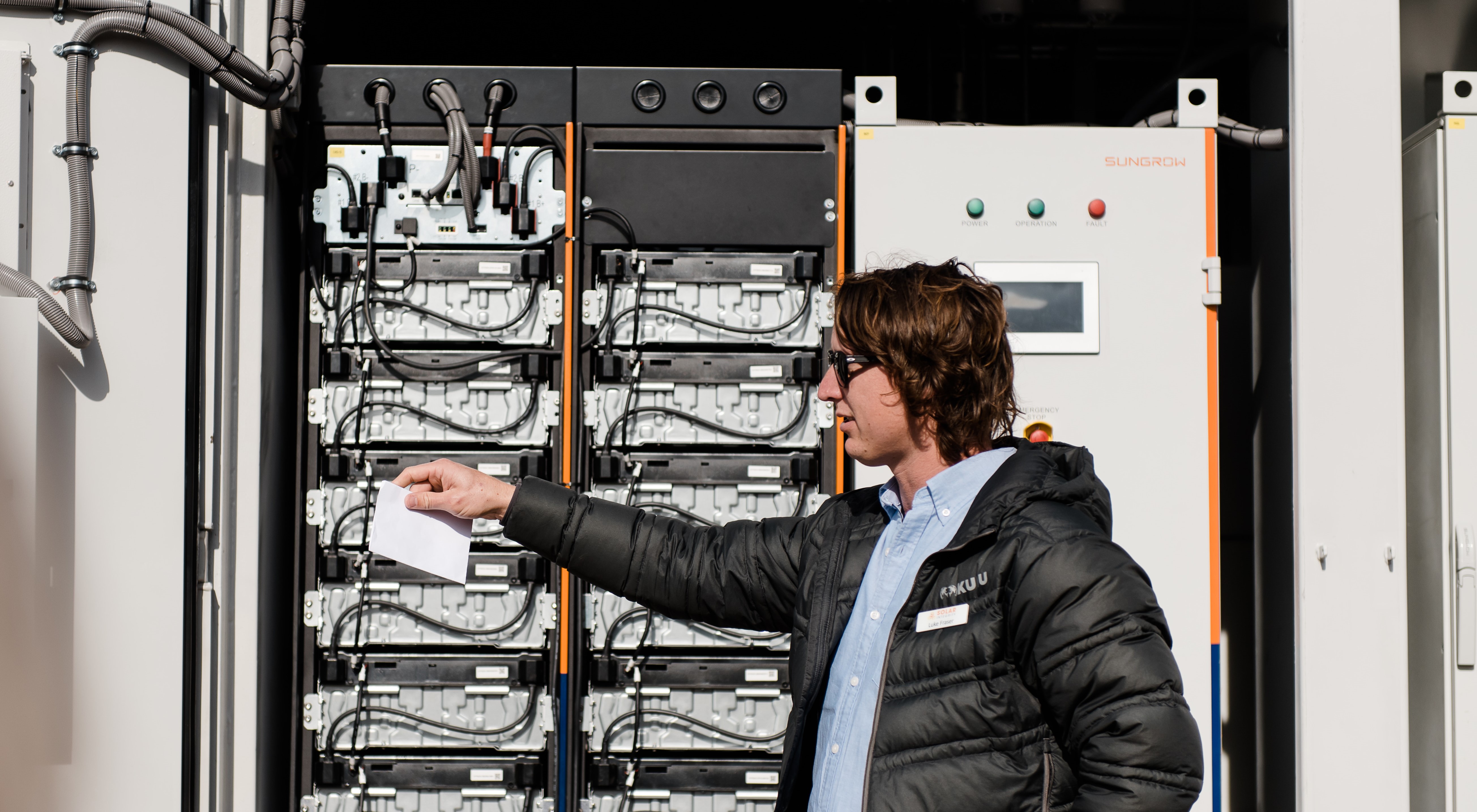 A man outside pointing to a large battery system